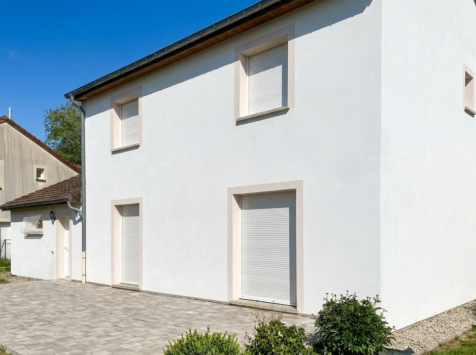 Façade d'une maison individuelle neuve, enduit blanc lisse, volets roulants blancs sur fenêtres et porte-fenêtre du rez-de-chaussée et étage