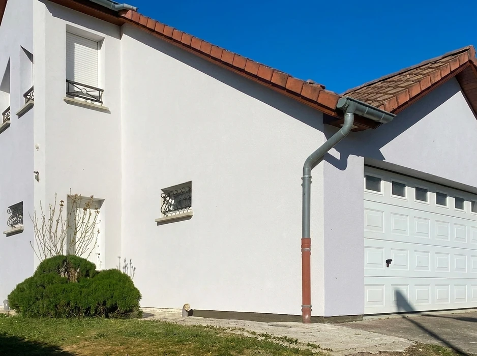 Façade blanche d'une maison individuelle avec garage attenant, toiture en tuiles canal terre cuite