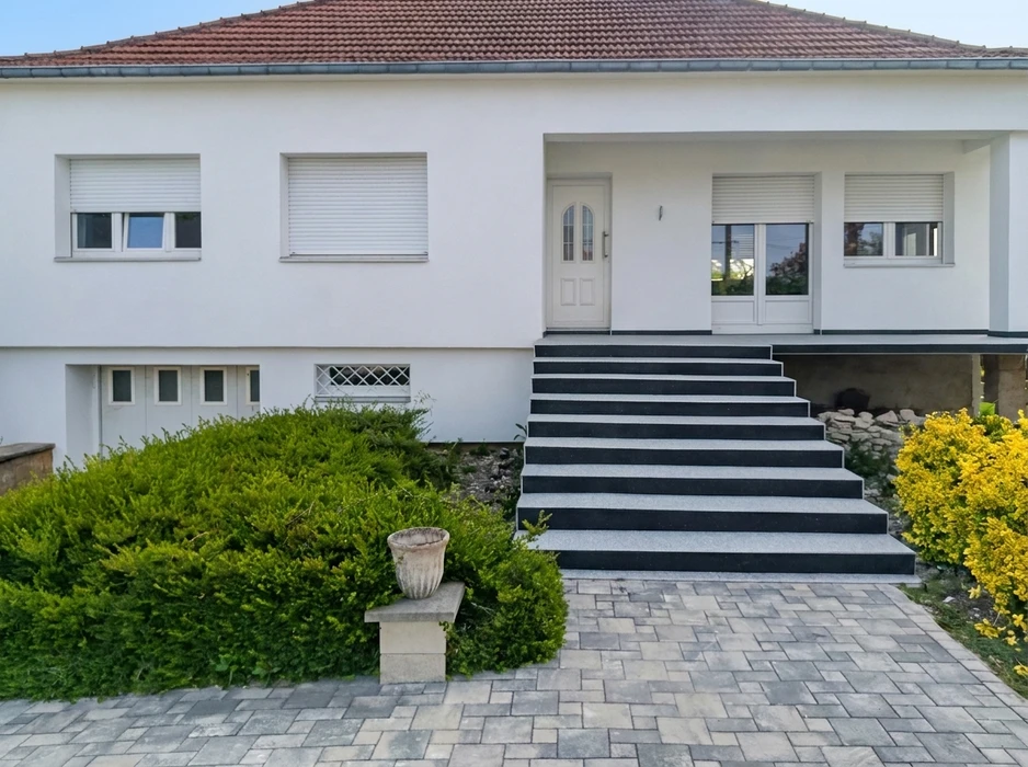 Façade de maison individuelle moderne, blanche, avec escalier d'entrée extérieur à 8 marches en granit bicolore : contremarches noires polies, girons gris flammés