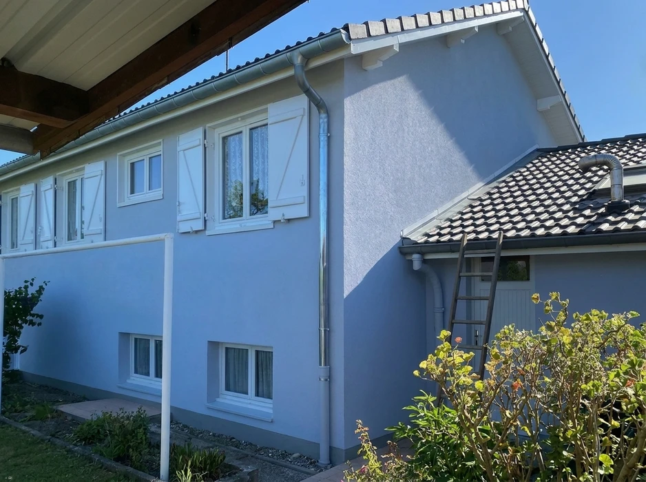 Façade extérieure d'une maison individuelle en crépi gris-bleu, vue d'angle