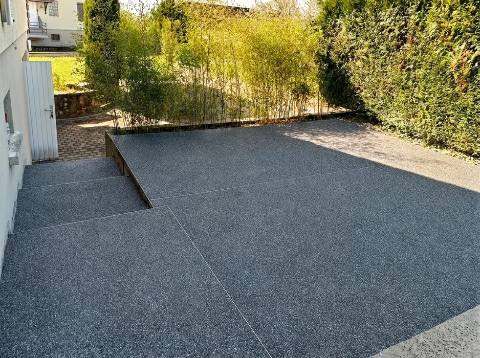 Terrasse extérieure avec revêtement en résine drainante gris anthracite, finition gravillonnée, avec joints de dilatation visibles