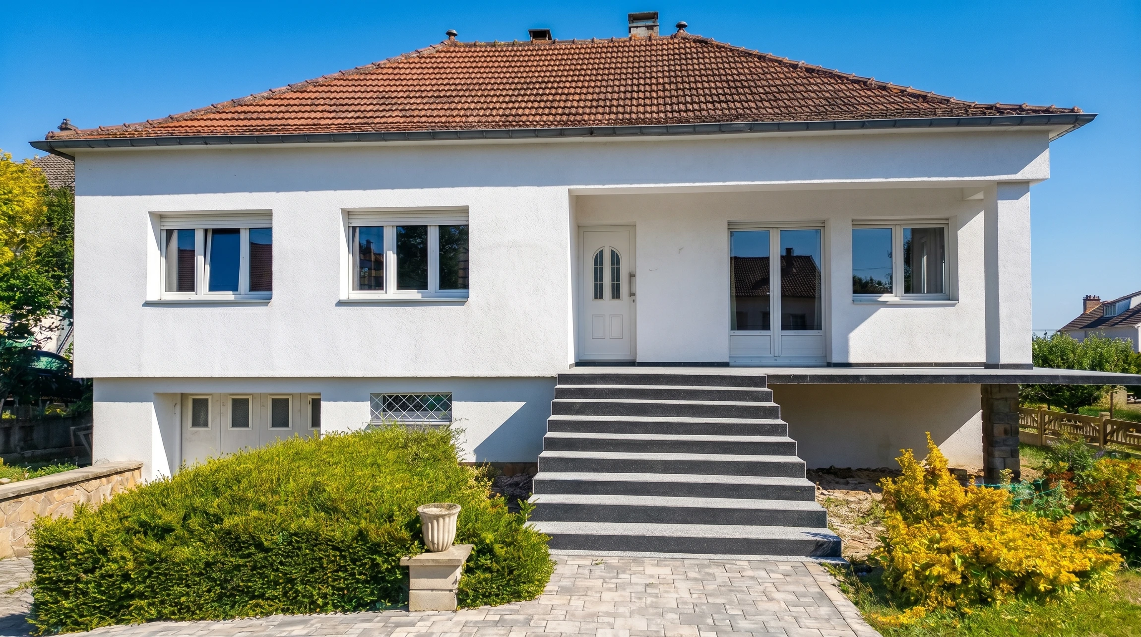 Ouvrier du bâtiment en vêtements de travail et casque blanc appliquant un enduit ou peinture blanche sur façade extérieure depuis échafaudage métallique