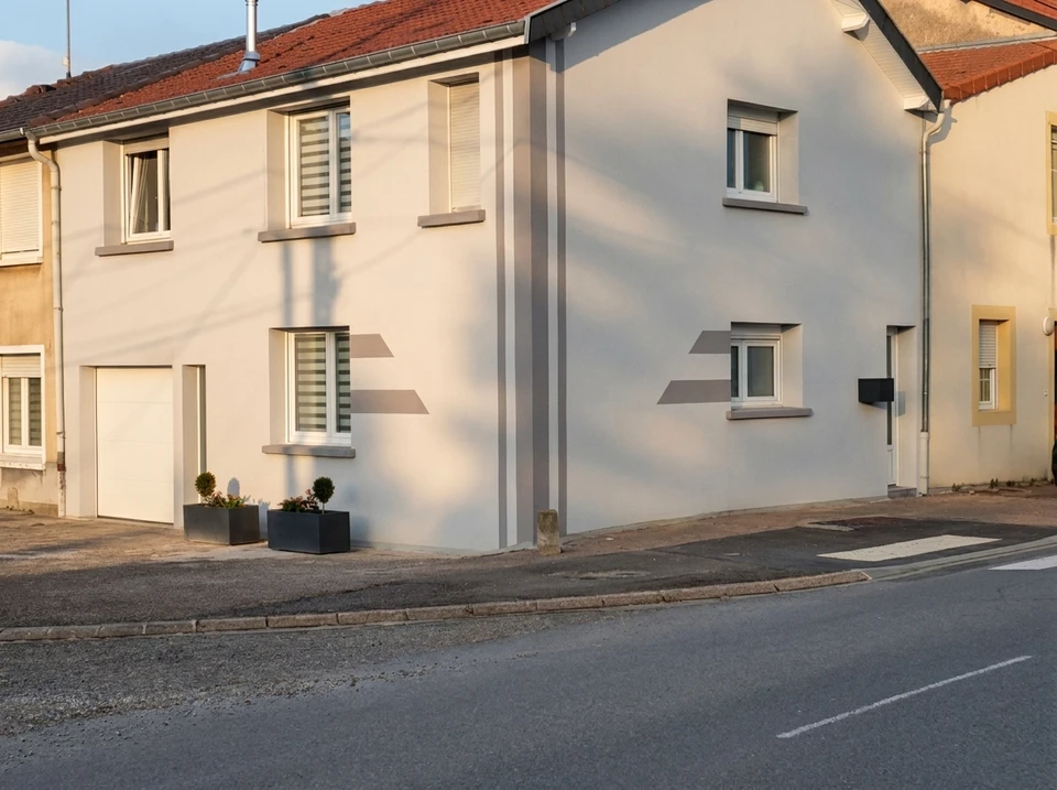 Artisan expérimenté en tenue de travail réalisant un ravalement de façade sur une maison individuelle régionale, utilisant les techniques professionnelles de nettoyage haute pression ou d'enduit, avec une façade partiellement rénovée montrant la différence avant/après, en contexte de chantier résidentiel en plein jour.